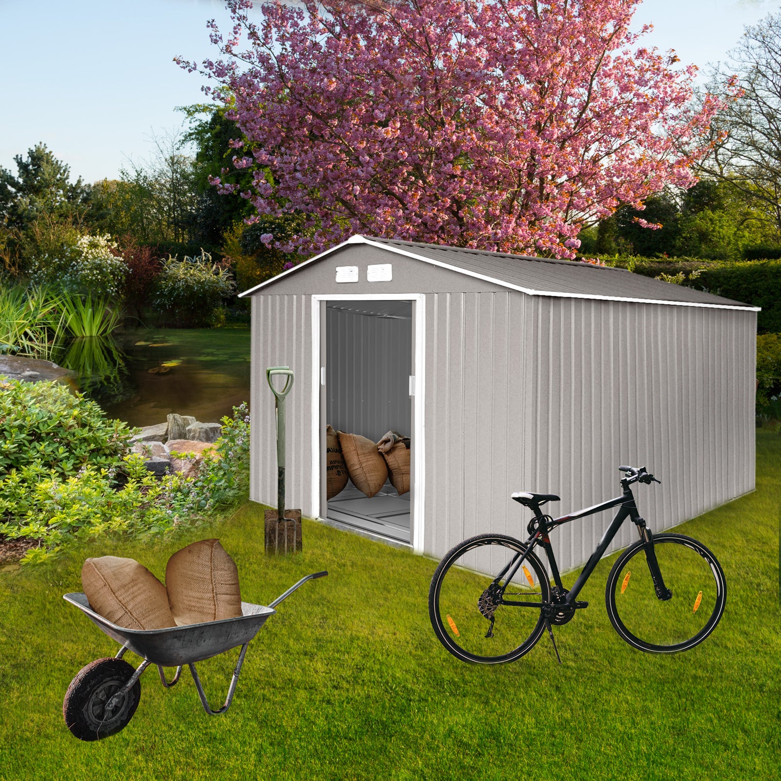 Grauer Metall-Gartenschuppen mit offener Tür, davor Schubkarre mit zwei Säcken, Spaten und schwarzes Fahrrad auf grünem Rasen, blühender Kirschbaum im Hintergrund