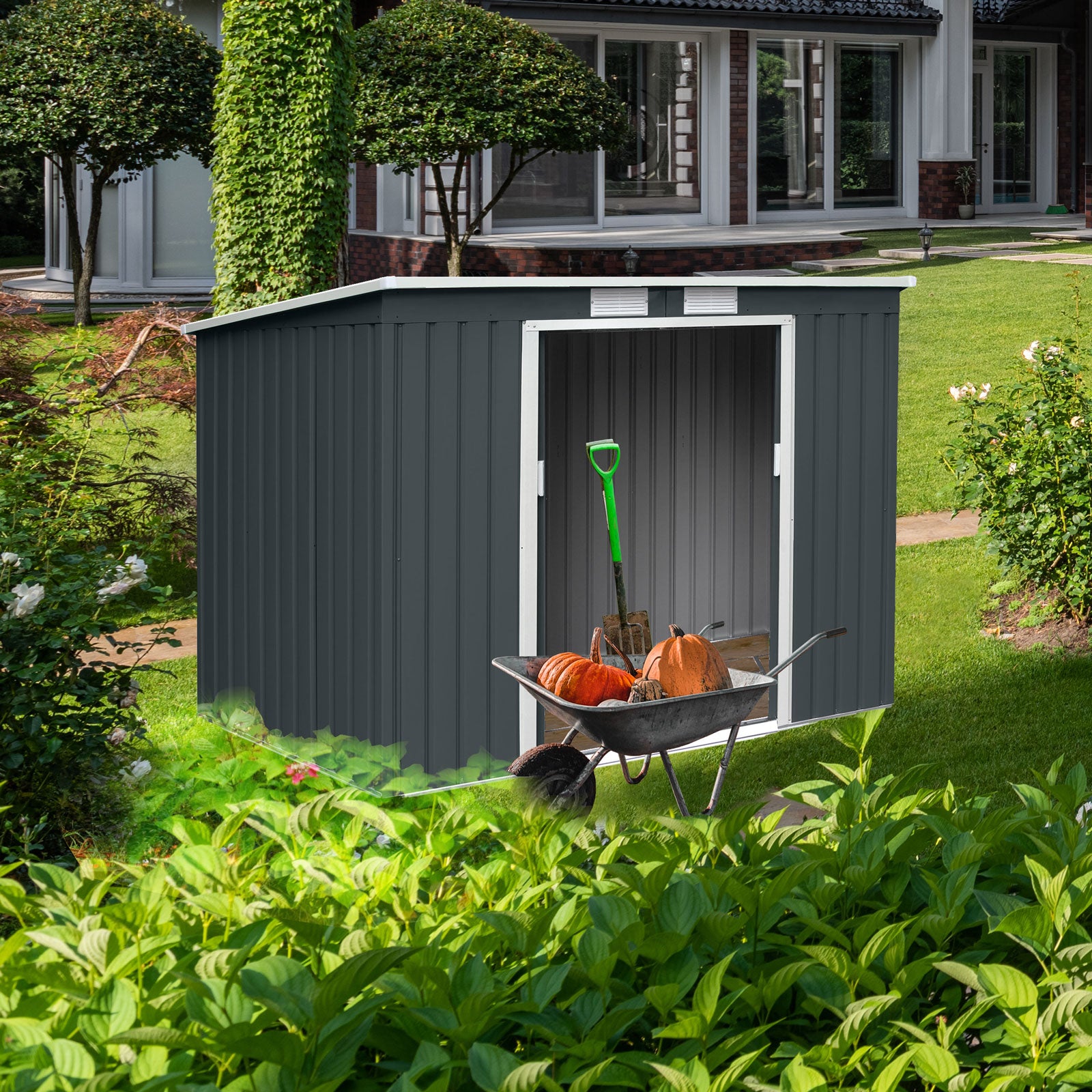 Grauer Gartenschuppen mit offenem Eingang, davor Schubkarre mit Kürbissen und grünem Spaten, umgeben von grünem Garten und Büschen